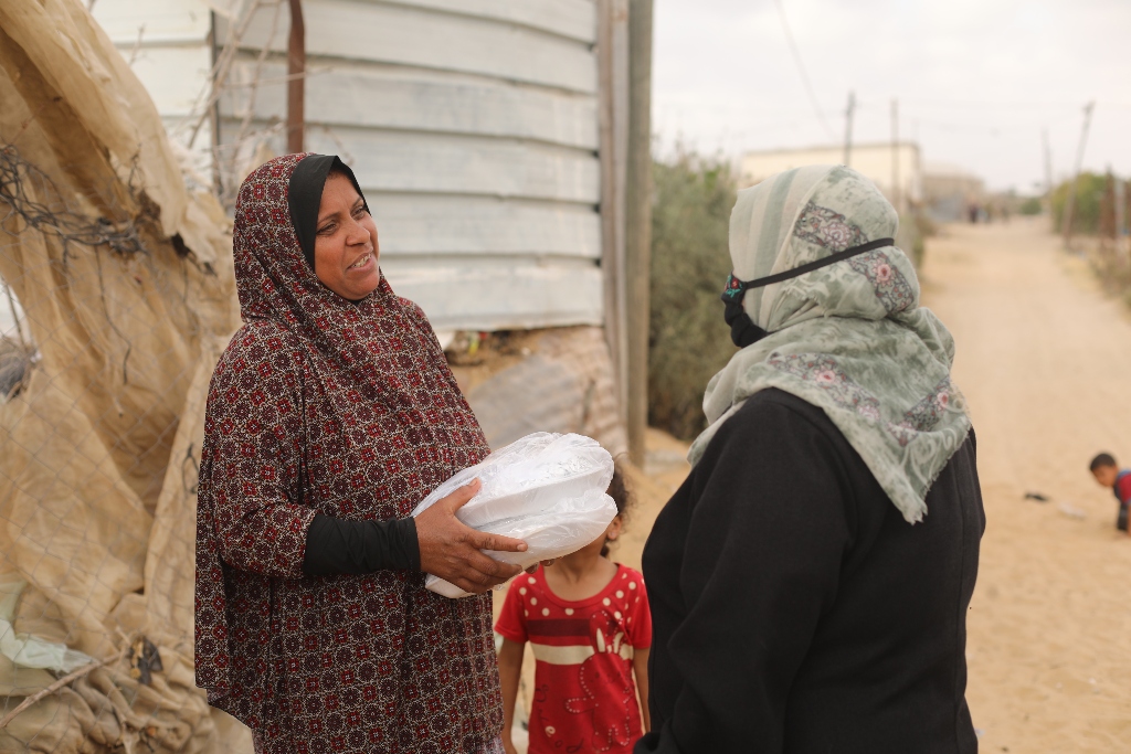 一位身边带着小女孩的妇女微笑着从Najah夫人手中接过两箱食物。