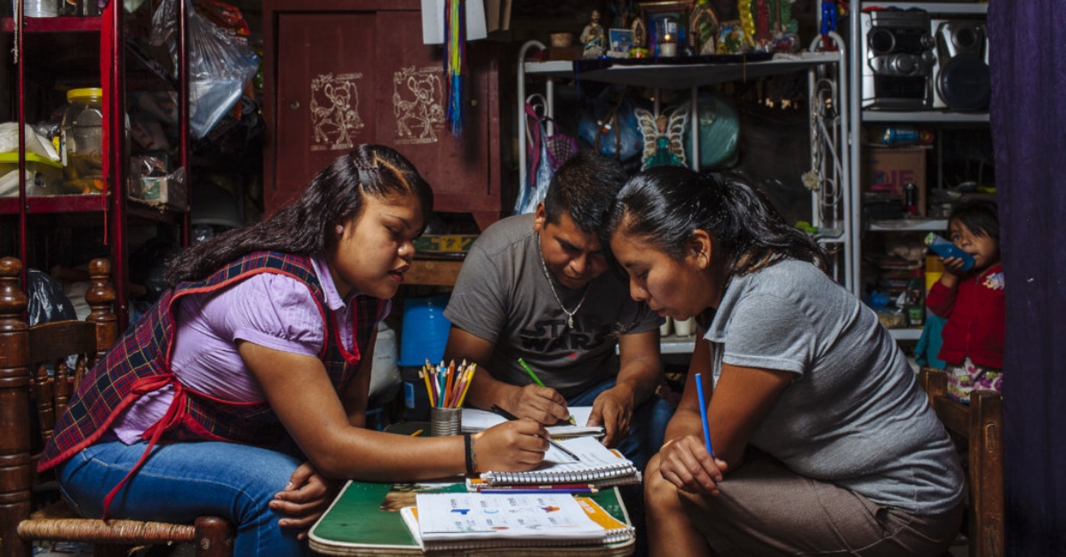 复杂的国际赠款。三个孩子坐在一张桌子旁，用彩色铅笔在笔记本上画画。