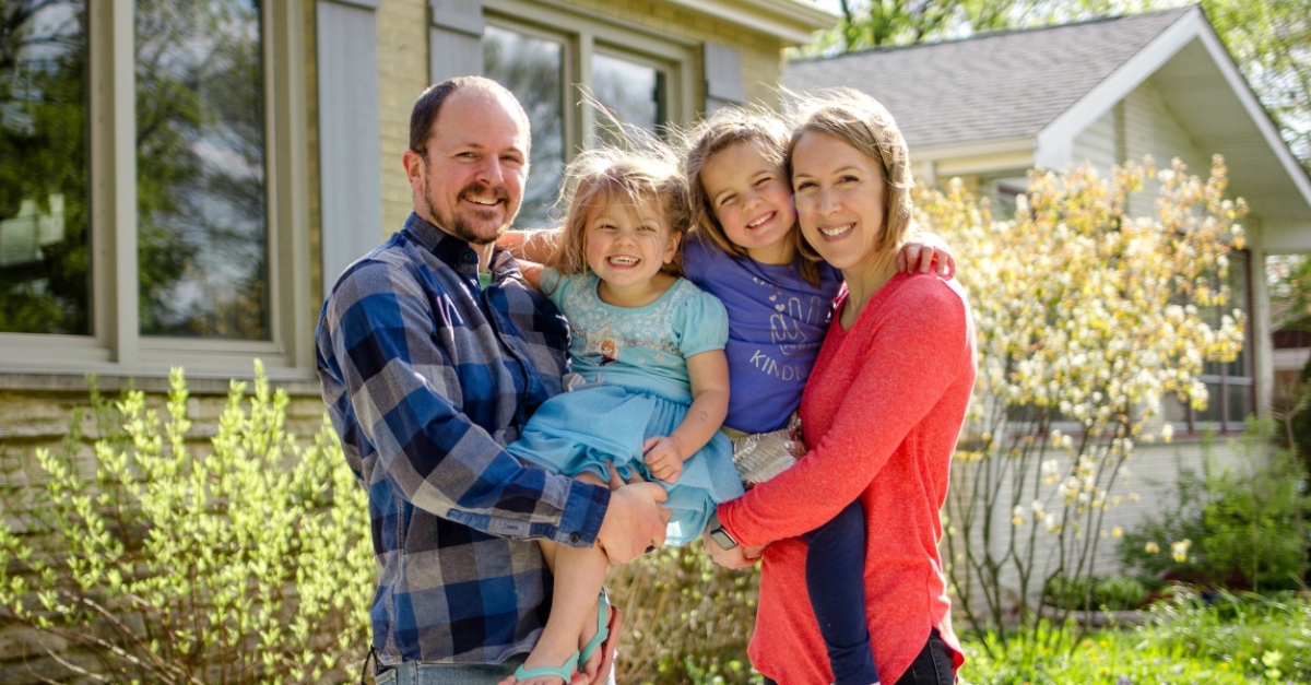 一名穿蓝色衣服的男子和一名穿红色衣服的妇女在一所房子前抱着两个年幼的女儿