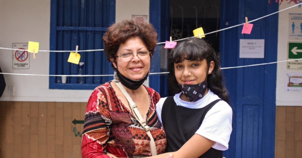 一个女人和一个小女孩一起站在一条晒衣绳前，晒衣绳上别着纸条。