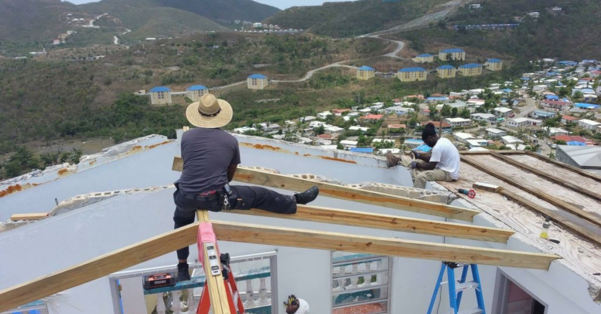 一位戴着宽边帽的建筑工人坐在部分建成的屋顶上俯瞰圣托马斯。另一个工人坐在框架的边缘。