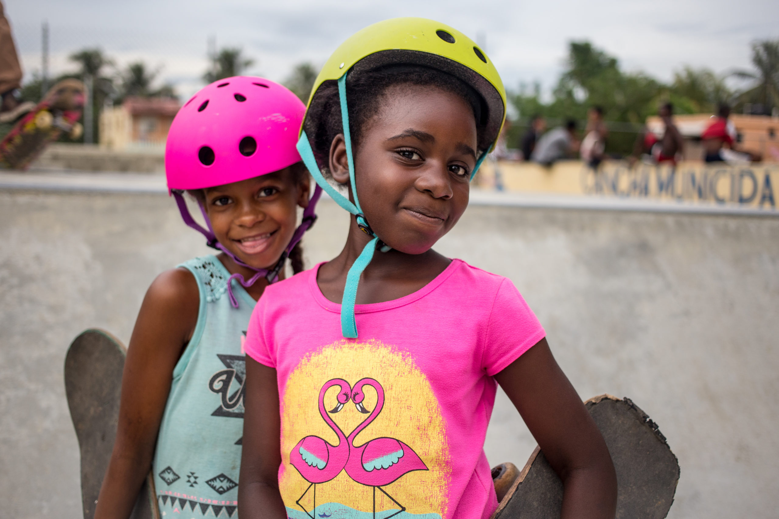两个戴着头盔的女孩，微笑着拿着滑板