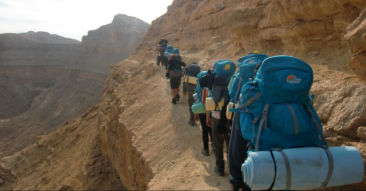 一队背着蓝色背包的背包客在悬崖边徒步旅行