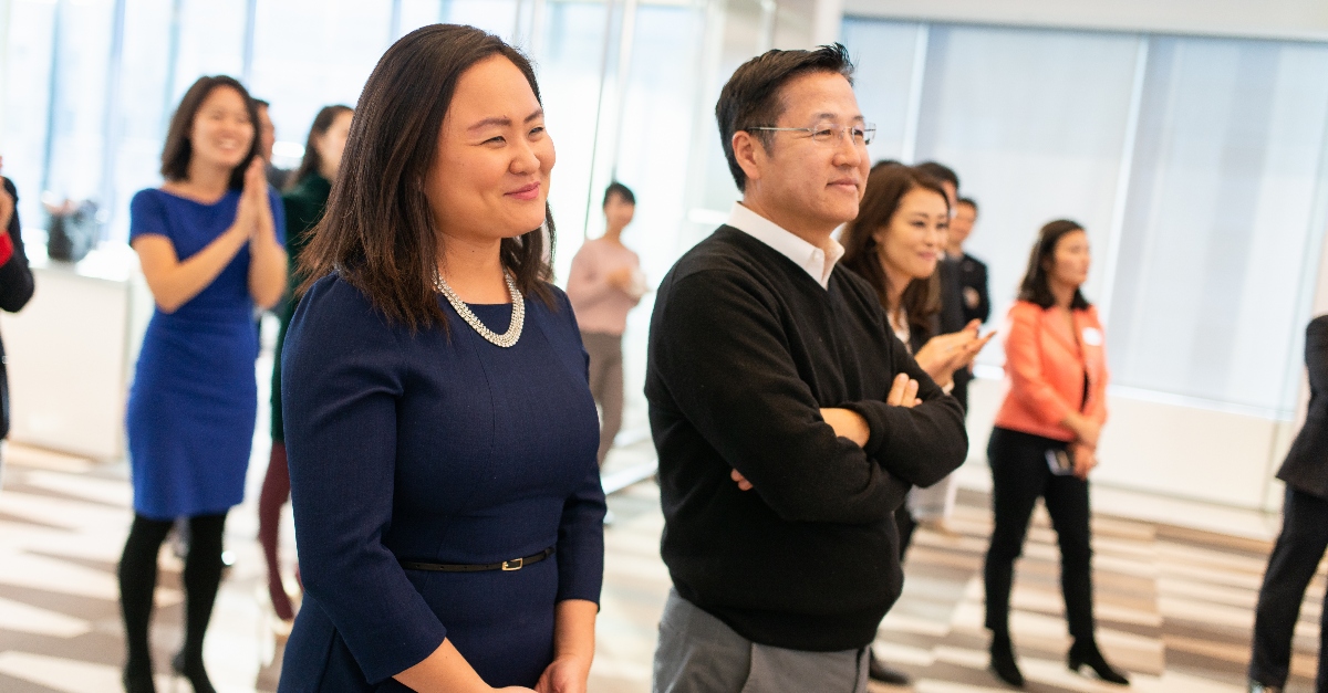 韩裔美国人协会的成员们站在一起参加一年一度的晚会。前景是一男一女，穿着商务装。