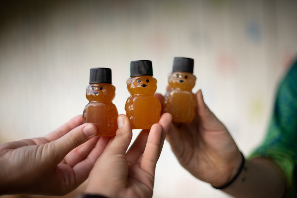 三个手举起小进小熊状的瓶子里的无刺的蜂蜜。