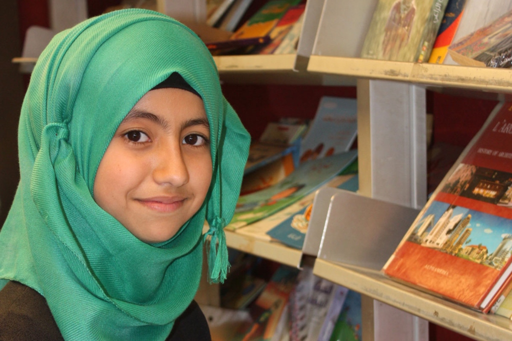 一个戴着绿色头巾的年轻女孩微笑着。书架在她身后