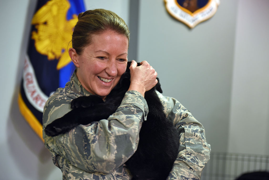 身着军装的女子抱着黑色的拉布拉多小狗。帮助退伍军人和服役人员的狗。