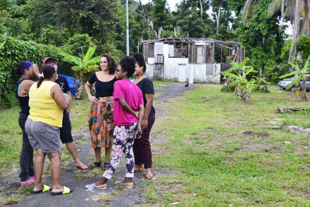 一群妇女站在一条砾石路上。他们身后是一座被飓风玛丽亚摧毁的白色房屋。