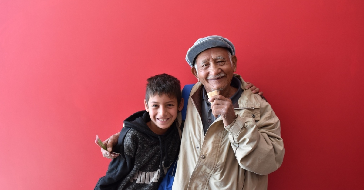 一位老人和一个小男孩在一堵红墙前微笑着拥抱在一起