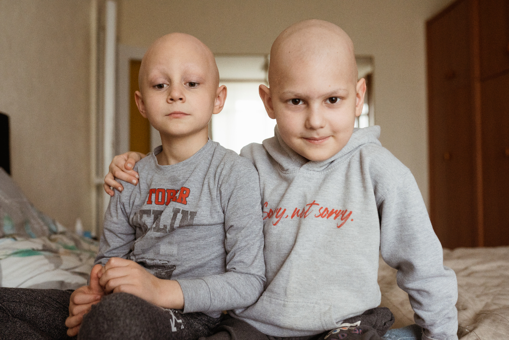 癌症病房的两个孩子坐在一起，一个手搭在另一个肩膀上，看着镜头
