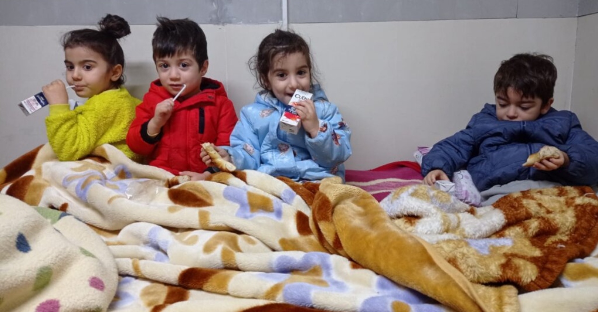小孩子们坐在一个空着的盒子下面，拿着果汁盒。如何帮助土耳其地震幸存者。