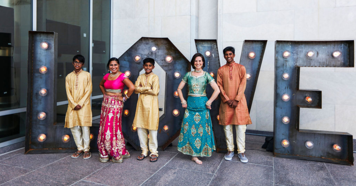 五人穿着庆祝印度衣服站在巨大的字母L O V E前婚礼慈善机构注册